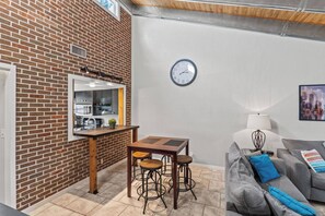 Un espace de vie compact comprenant un coin cuisine, une table à manger avec des tabourets et un coin salon avec un canapé et des coussins.