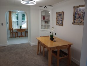 En matplats med ett träbord och stolar, ett vitt skåp med glasdörrar och en taklampa.