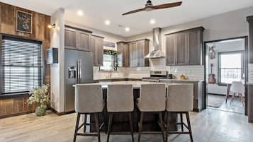 A modern kitchen with a central island, bar stools, a ceiling fan, and a view of a guitar in the adjacent room.