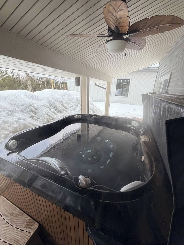 A hot tub with a ceiling fan above it, set against a snowy landscape.