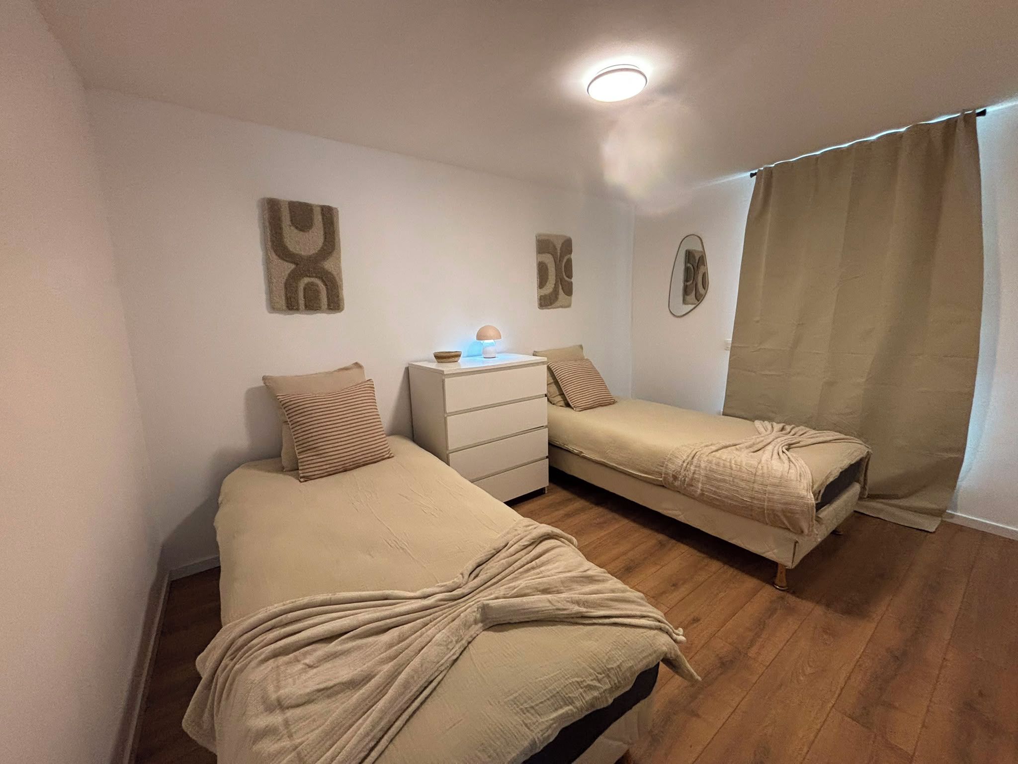Een slaapkamer met twee bedden, een nachtkastje met een lamp en een raam met gordijnen.