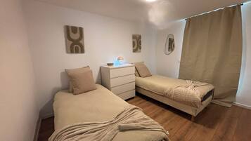 Een slaapkamer met twee bedden, een nachtkastje met een lamp en een raam met gordijnen.