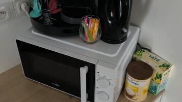 Een magnetron op een houten aanrecht, met een koffiezetapparaat, een mok, een suikerpot en een pak YATE instantkoffie.