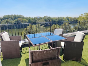 Ein Sitzbereich im Freien mit Tisch und Stühlen mit Blick auf ein Gewässer und Grünflächen.