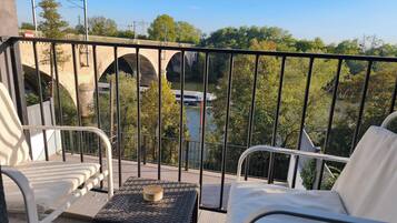A balcony with a view of a bridge and river, furnished with two white chairs and a small table.