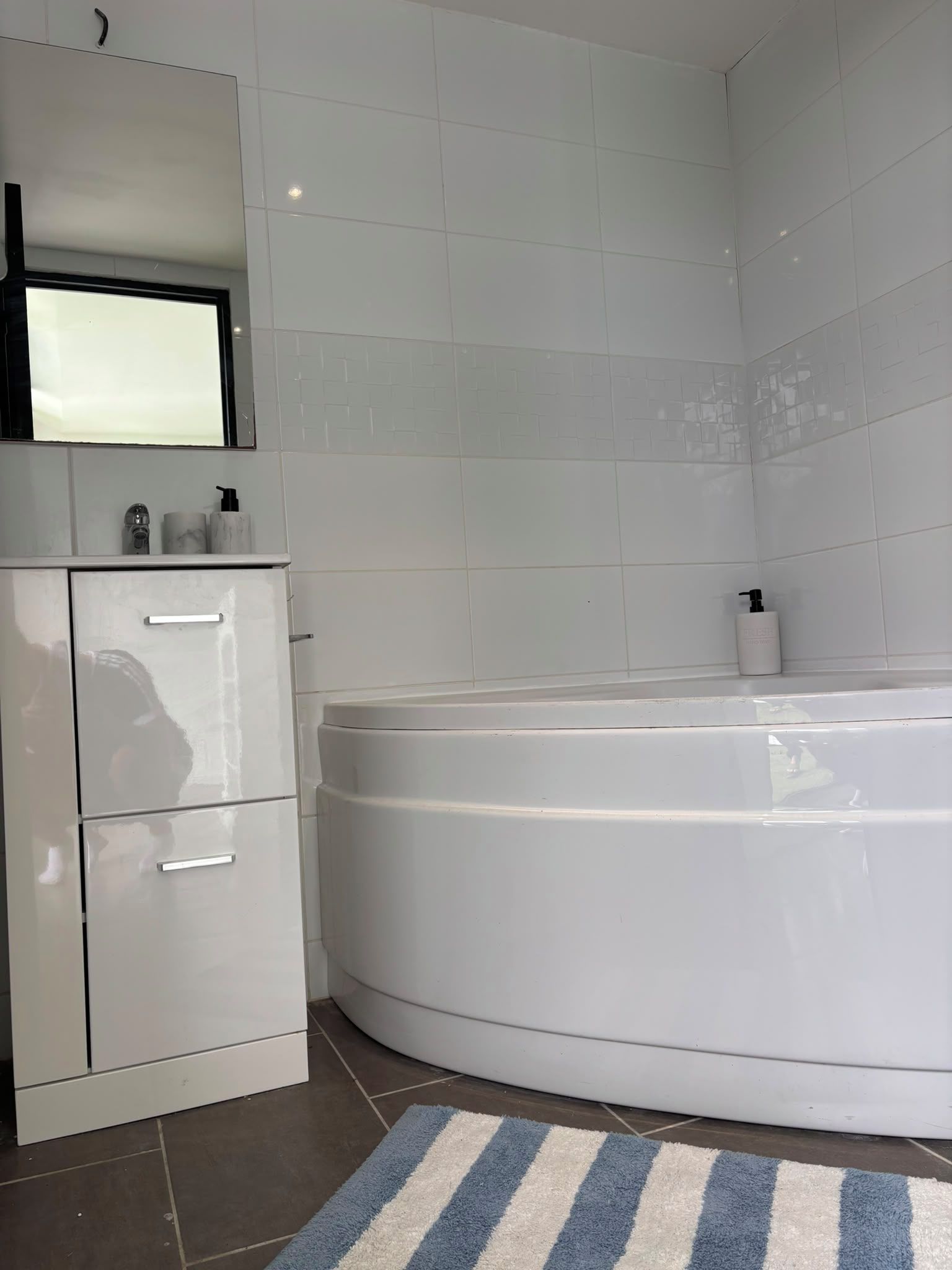 A modern bathroom with a white bathtub, a vanity with a mirror, and a striped rug.