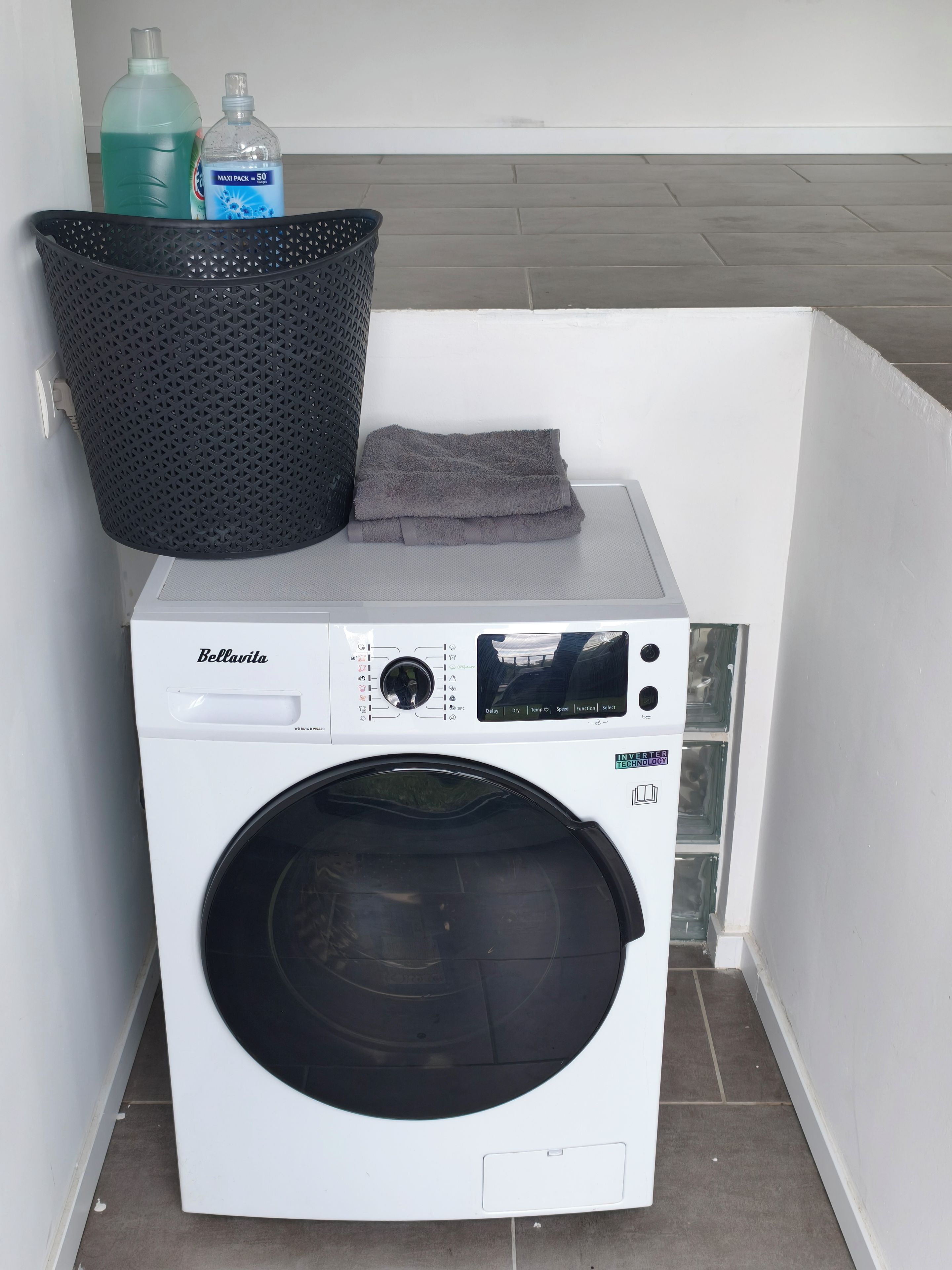 Un lave-linge à chargement frontal doté d’un panneau de commande, d’un panier à linge noir et de deux bouteilles de lessive liquide posées sur le dessus.