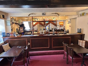 A bar area with a wooden counter, seating with cushioned benches, and a variety of bottles and glasses. - The Ganton Greyhound (Scarborough)