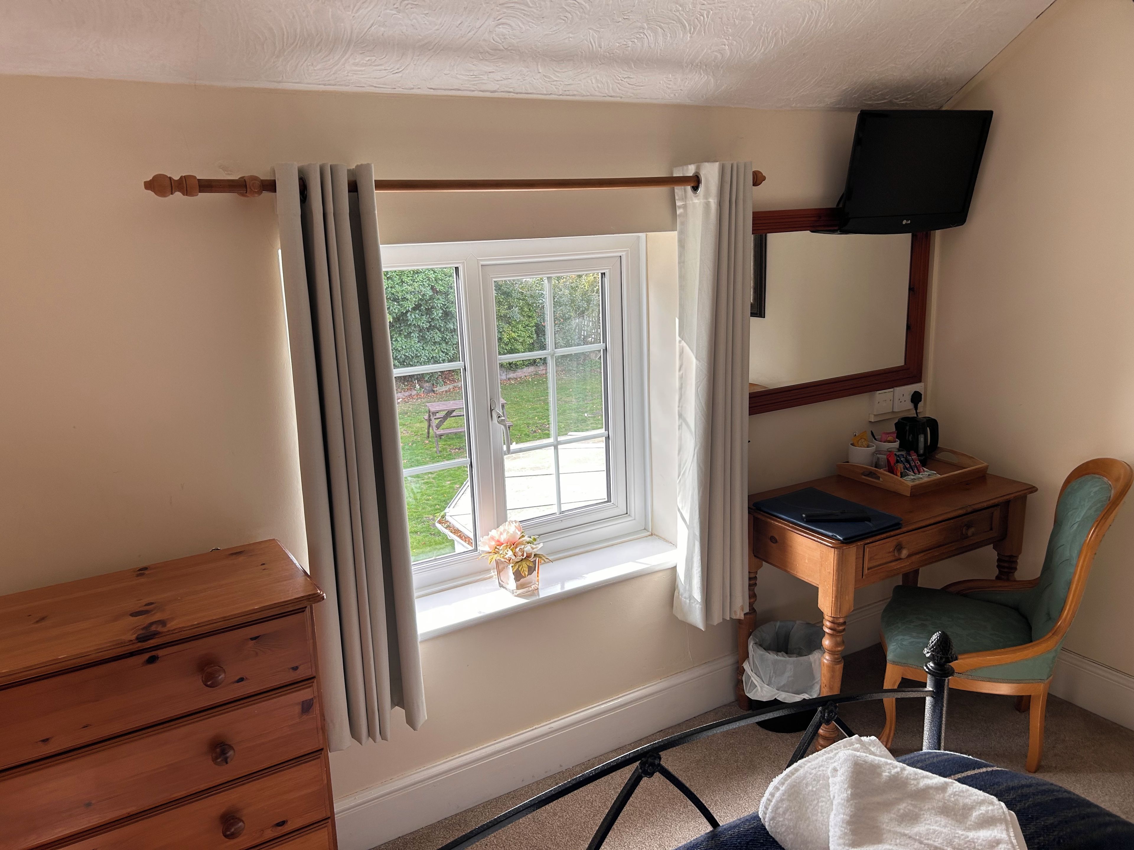 Una habitación con un aparador de madera, un escritorio con silla, una ventana con cortinas y un televisor colgado en la pared.