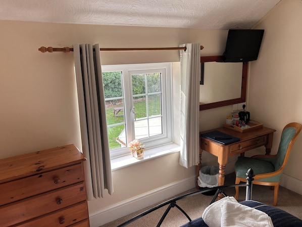 A room with a wooden dresser, a desk with a chair, a window with curtains, and a television mounted on the wall. - The Ganton Greyhound (Scarborough)