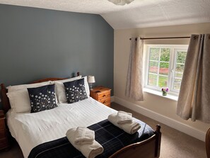 A bedroom with a bed, pillows, a bedside table, a lamp, a window with curtains, and a view of the outside.