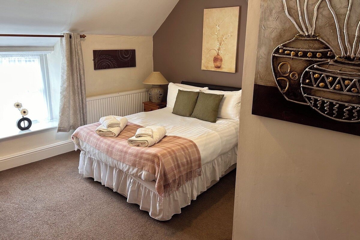 A bedroom with a bed, a window with curtains, a lamp, and a wall art piece.