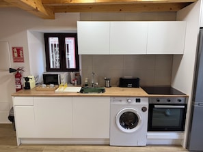 A compact kitchen with a washing machine, oven, microwave, and toaster.