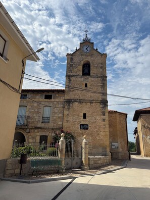 A historic stone building with a clock tower, a sign indicating a protected site, and a bench in the foreground.