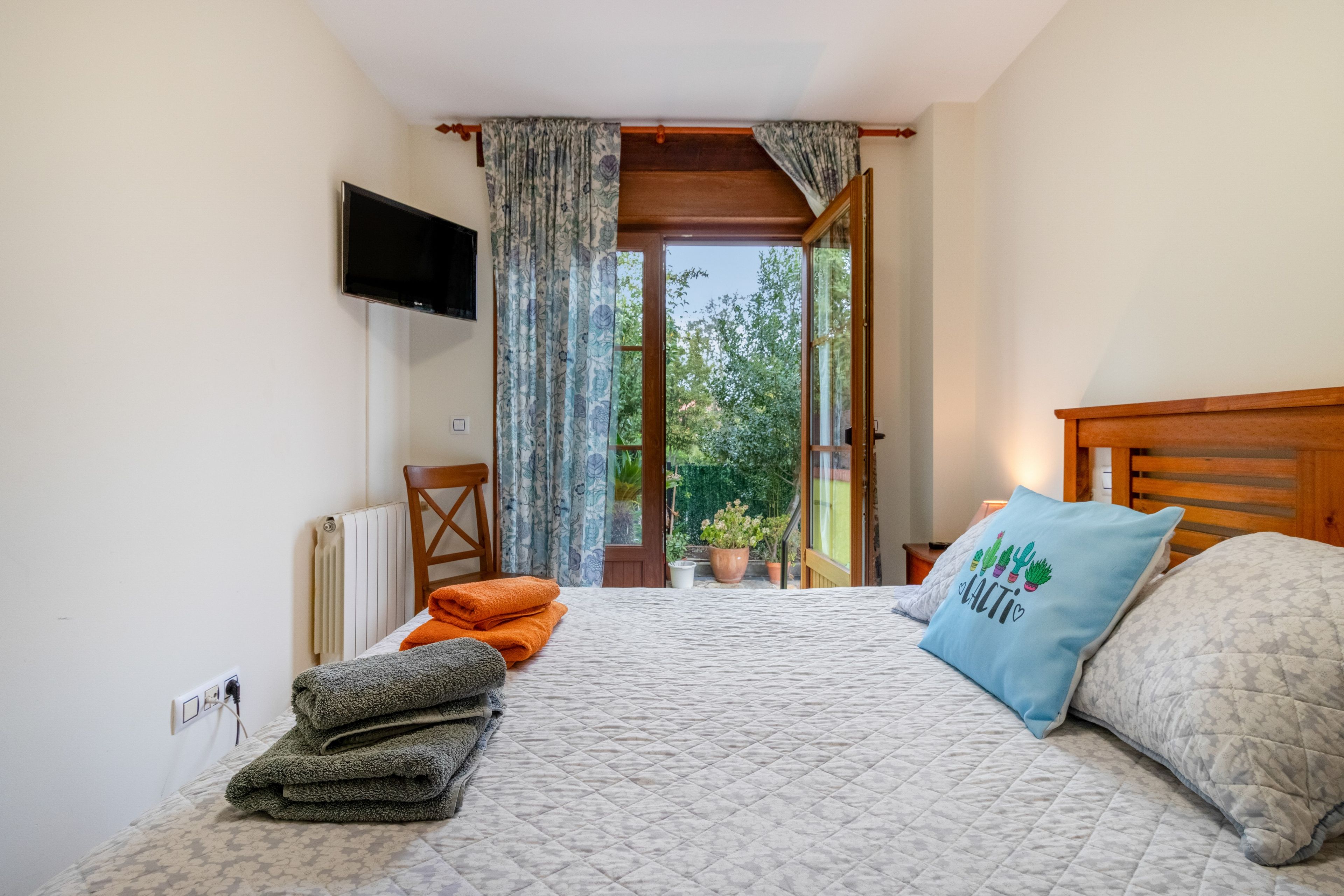A bedroom with a bed, a TV, a window with curtains, and a view of greenery outside.