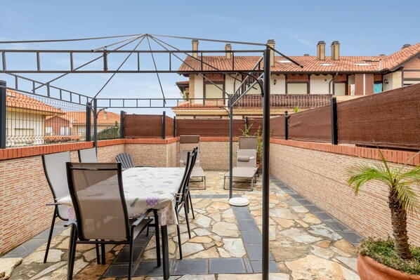 A patio area with a table and chairs, a covered seating area, and a view of a residential building in the background.