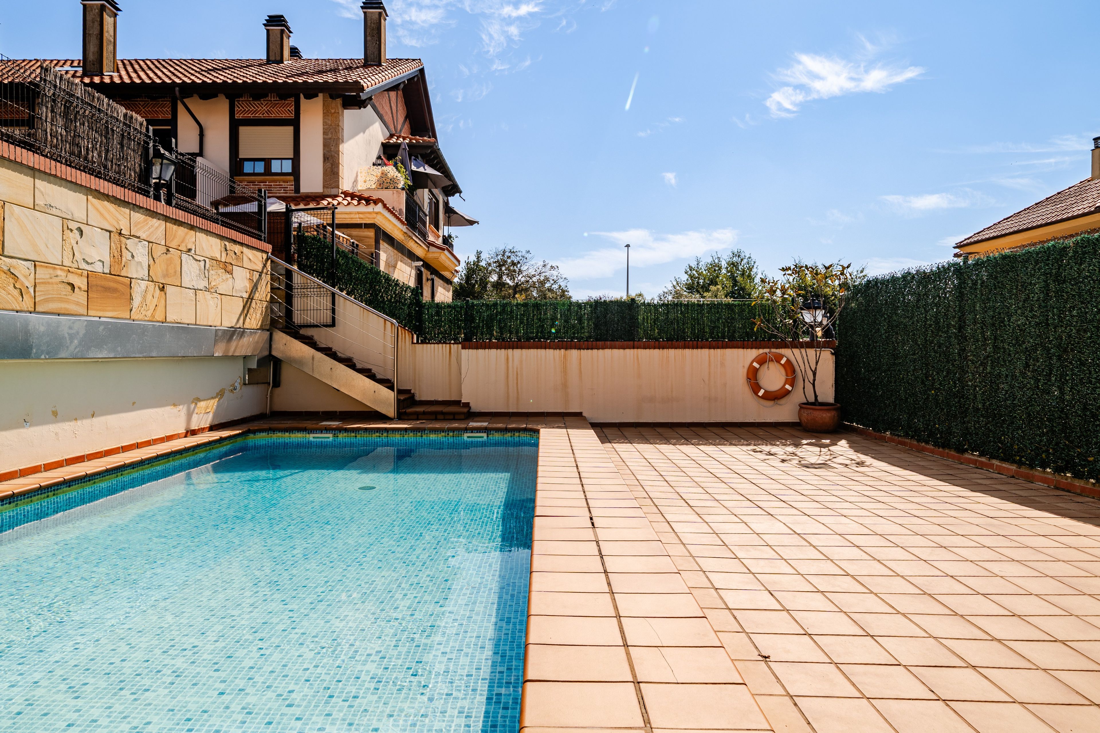 Una piscina con bordes de cerámica, una pared de piedra y un seto.