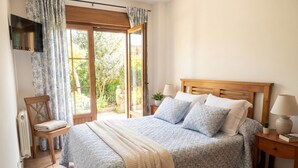 Ein Schlafzimmer mit Bett, Stuhl, Nachttisch, Lampe und Blick ins Grüne durch ein Fenster.
