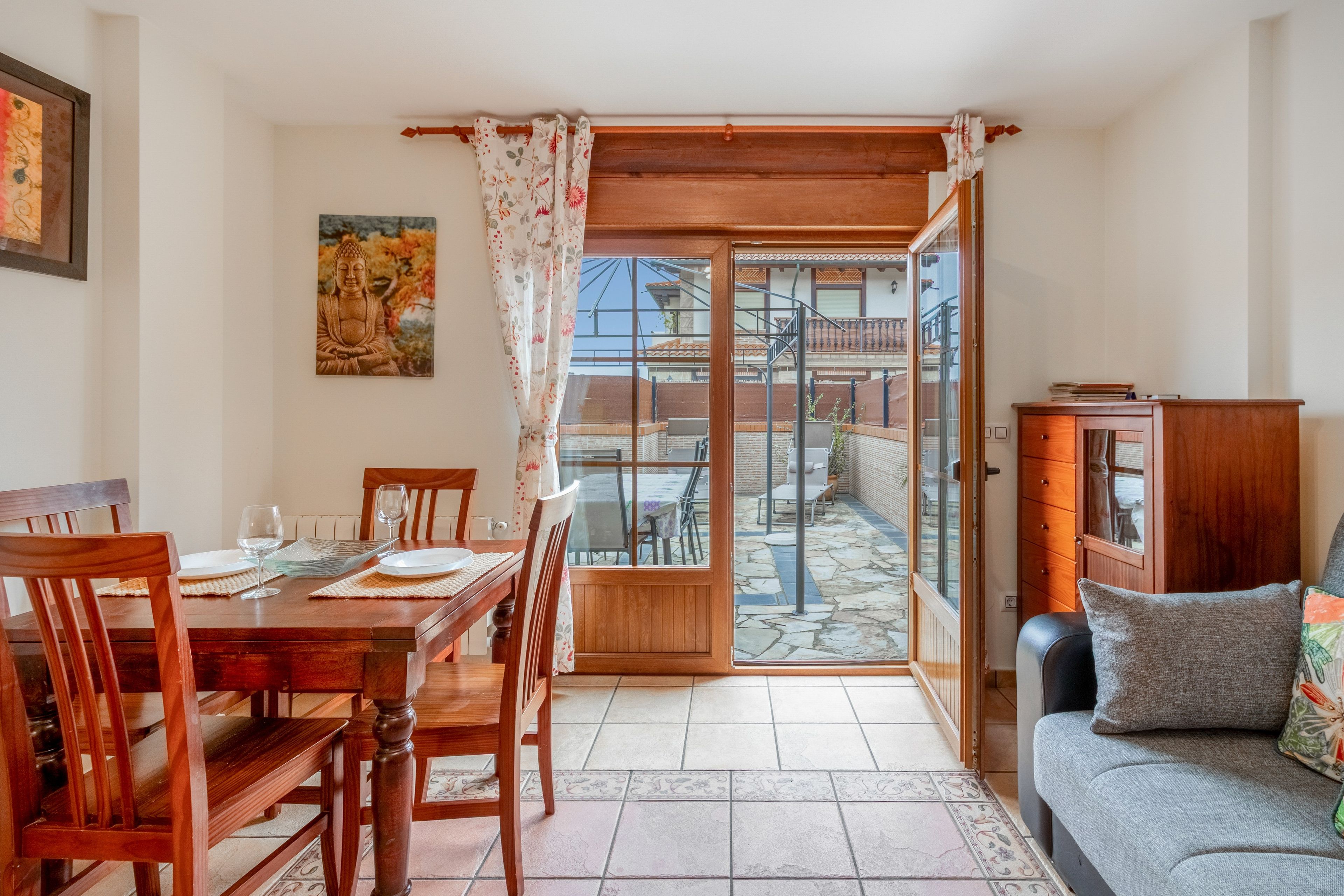 Un comedor con mesa y sillas de madera, un sofá y vistas al balcón exterior a través de un ventanal.