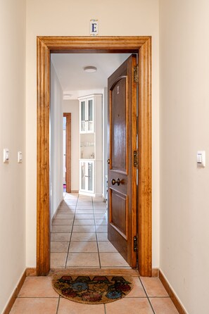 A hallway with a wooden door, a tiled floor, and a rug at the entrance.
