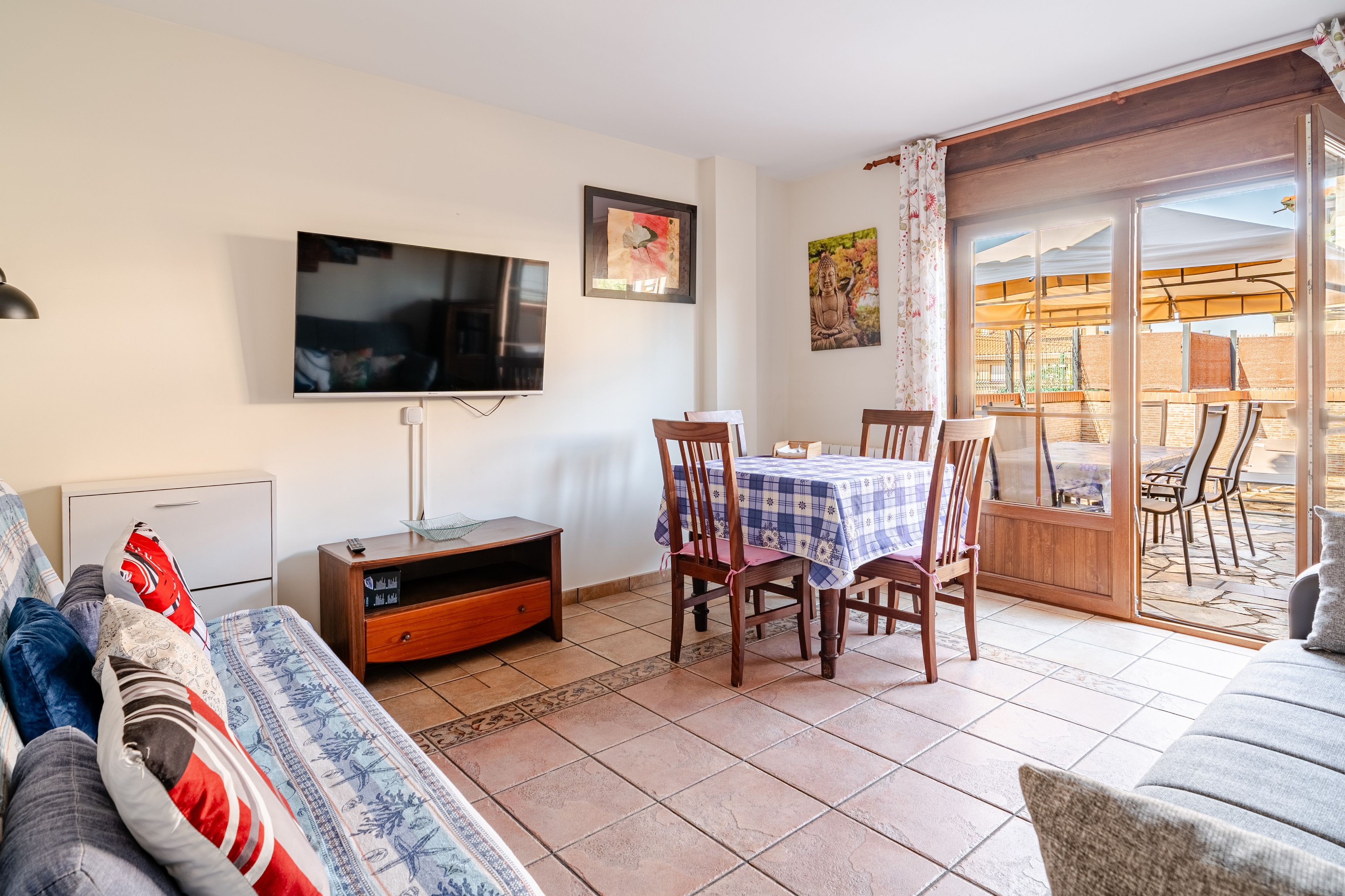 Ein Wohnzimmer mit Fernseher, einer Couch, einem Esstisch mit Stühlen und einer Glastür zum Außenbereich.