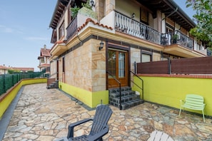 Un edificio de dos plantas con un patio de piedra, una puerta de madera y una silla verde.