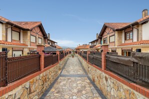 A pathway flanked by buildings with red-tiled roofs, stone walls, and metal fences.