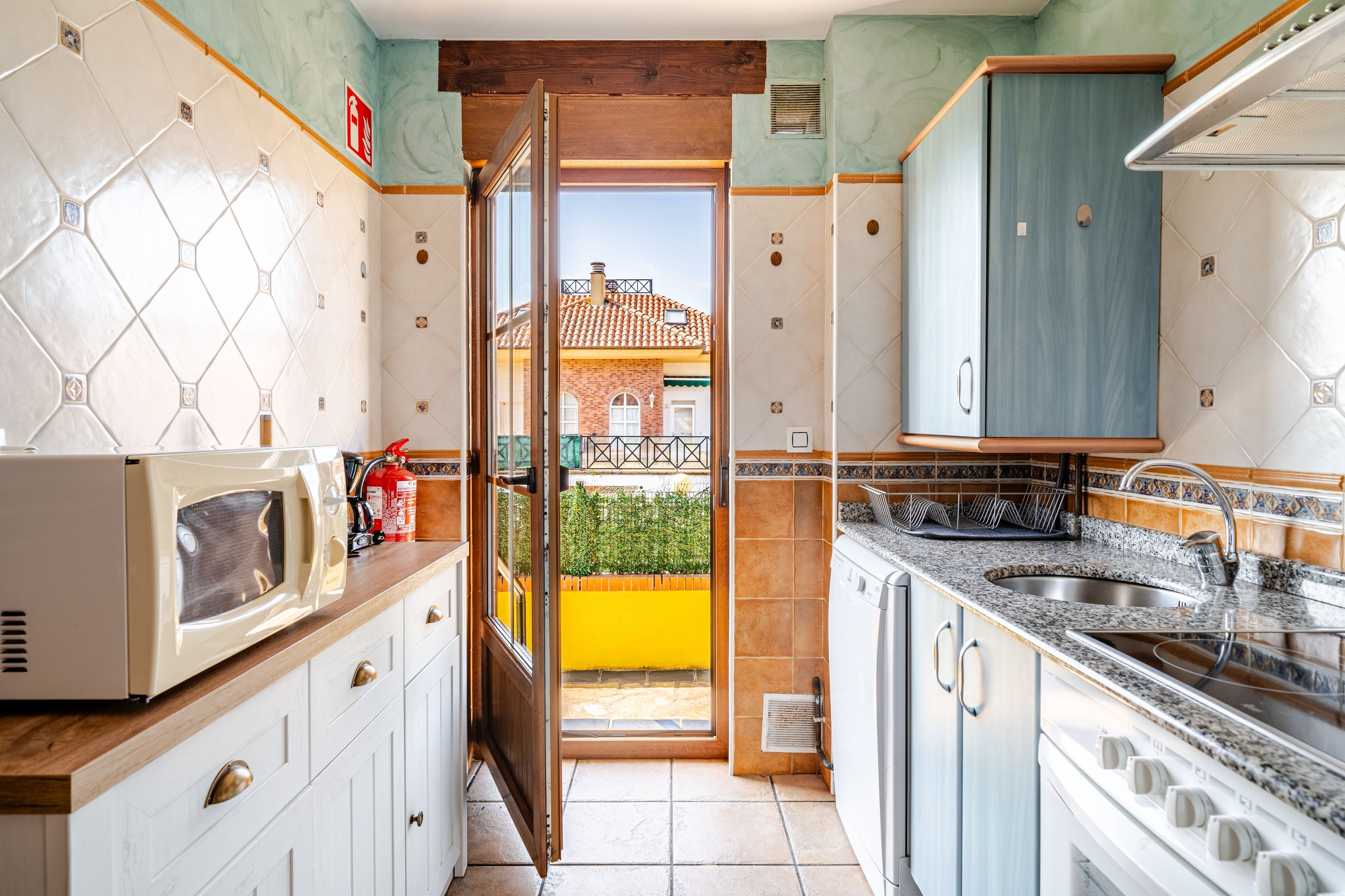 A kitchen with a view to the outside, featuring a microwave, stove, sink, and cabinets.