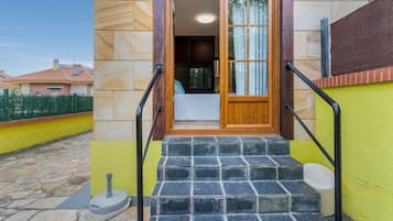 A set of stone steps leading to a wooden door with a glass panel, a metal handrail on each side, and a small outdoor area with a stone floor.