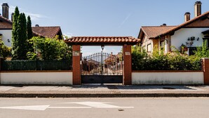 Ein verschlossenes Einfahrtstor zu einer Wohngegend mit Ziegelmauer und Metallgitter, bewölkter Himmel.