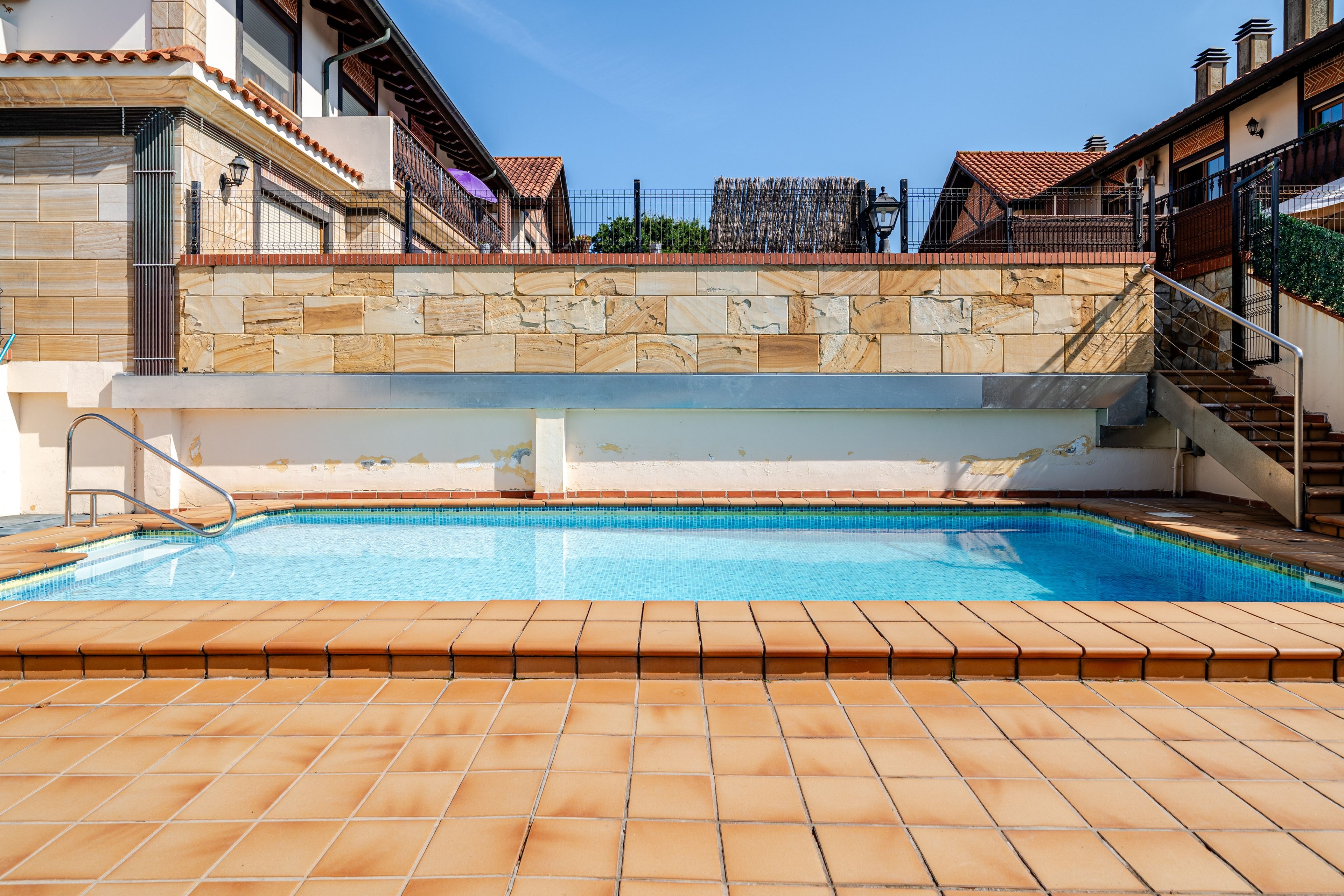 Ein Swimmingpool mit Steinmauer und gefliestem Deck, umgeben von Gebäuden mit Balkonen.