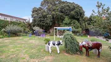 Een tuin met een schommel, een koeienbeeld en een paardenbeeld.