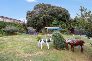 A garden with a swing set, a statue of a cow, and a statue of a horse.