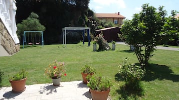 A courtyard with a swing set, a gazebo, potted plants, and a stone wall.