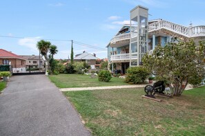A residential property with a paved driveway, a grassy lawn, and a variety of potted plants.