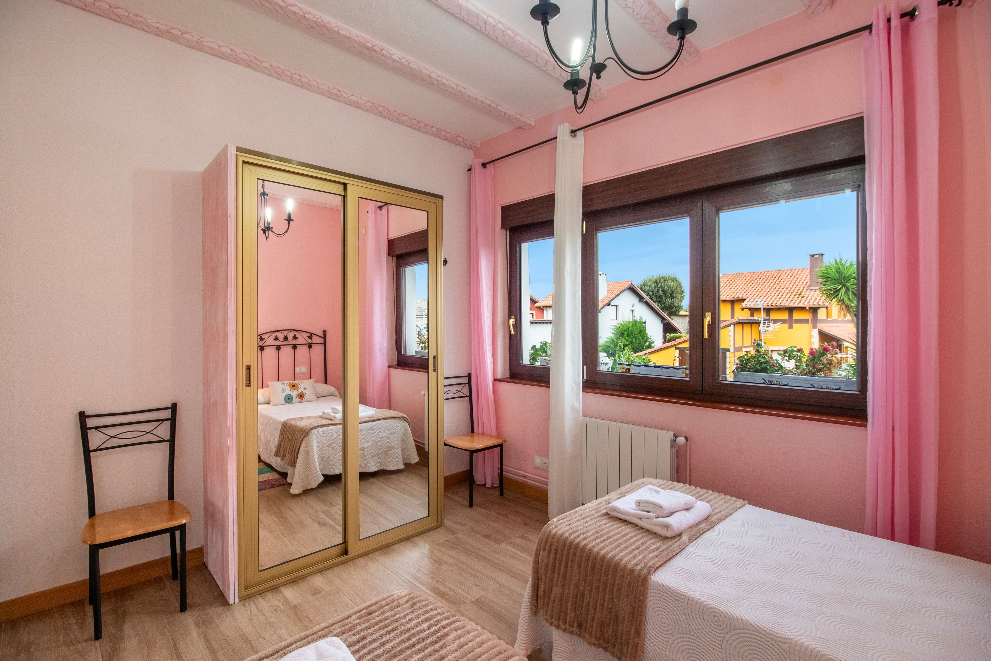 Een slaapkamer met een bed, een stoel, een spiegel en een raam met uitzicht op huizen.
