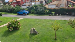 A residential area with a blue car parked on the street, well-maintained lawns, and a variety of shrubs and flowers.