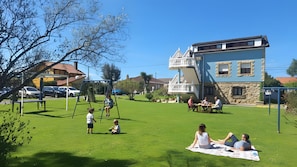 Un espacio al aire libre con césped, un conjunto de columpios, una mesa de picnic y un edificio con balcón.