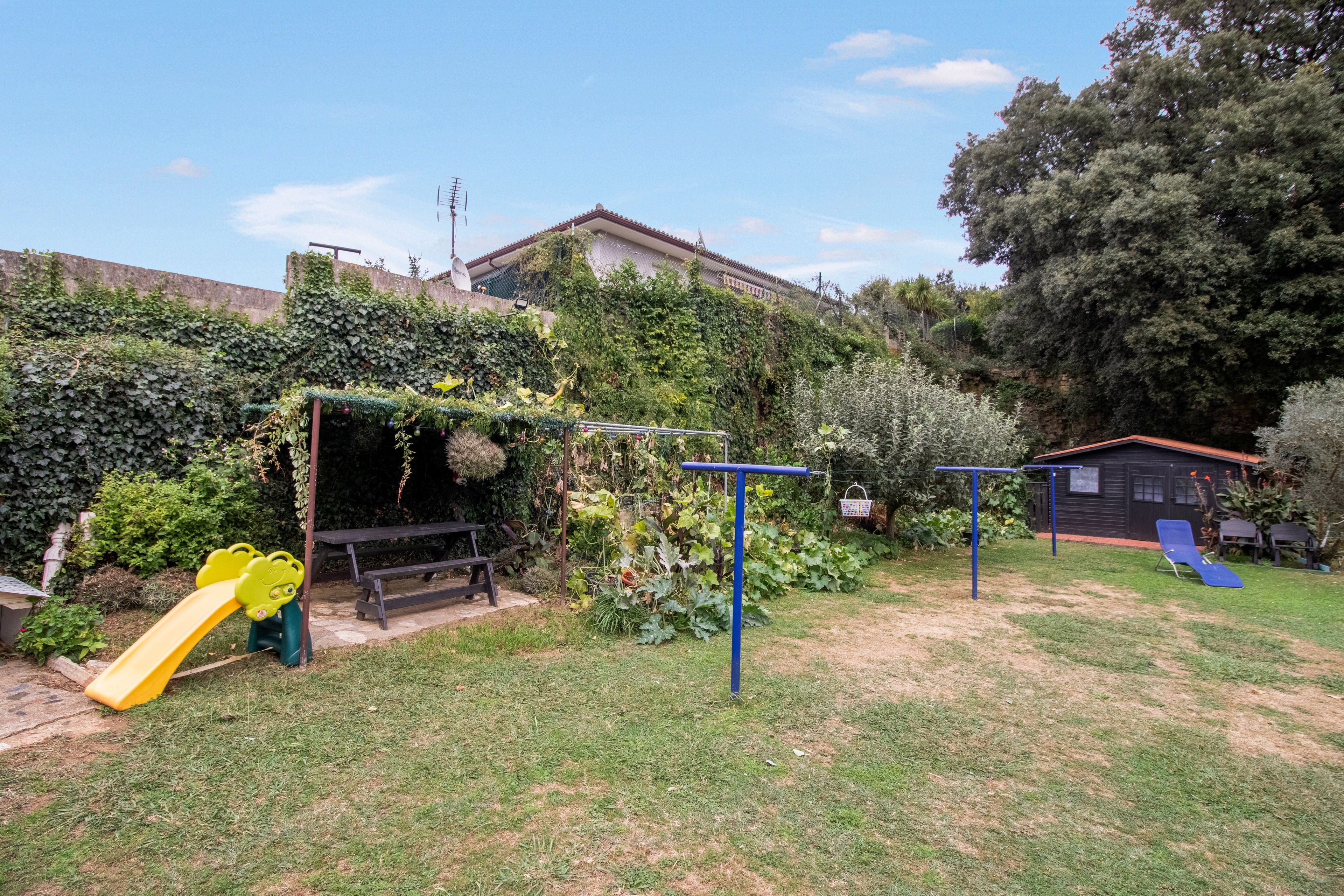 A backyard with a play area including a slide, swings, and a bench.