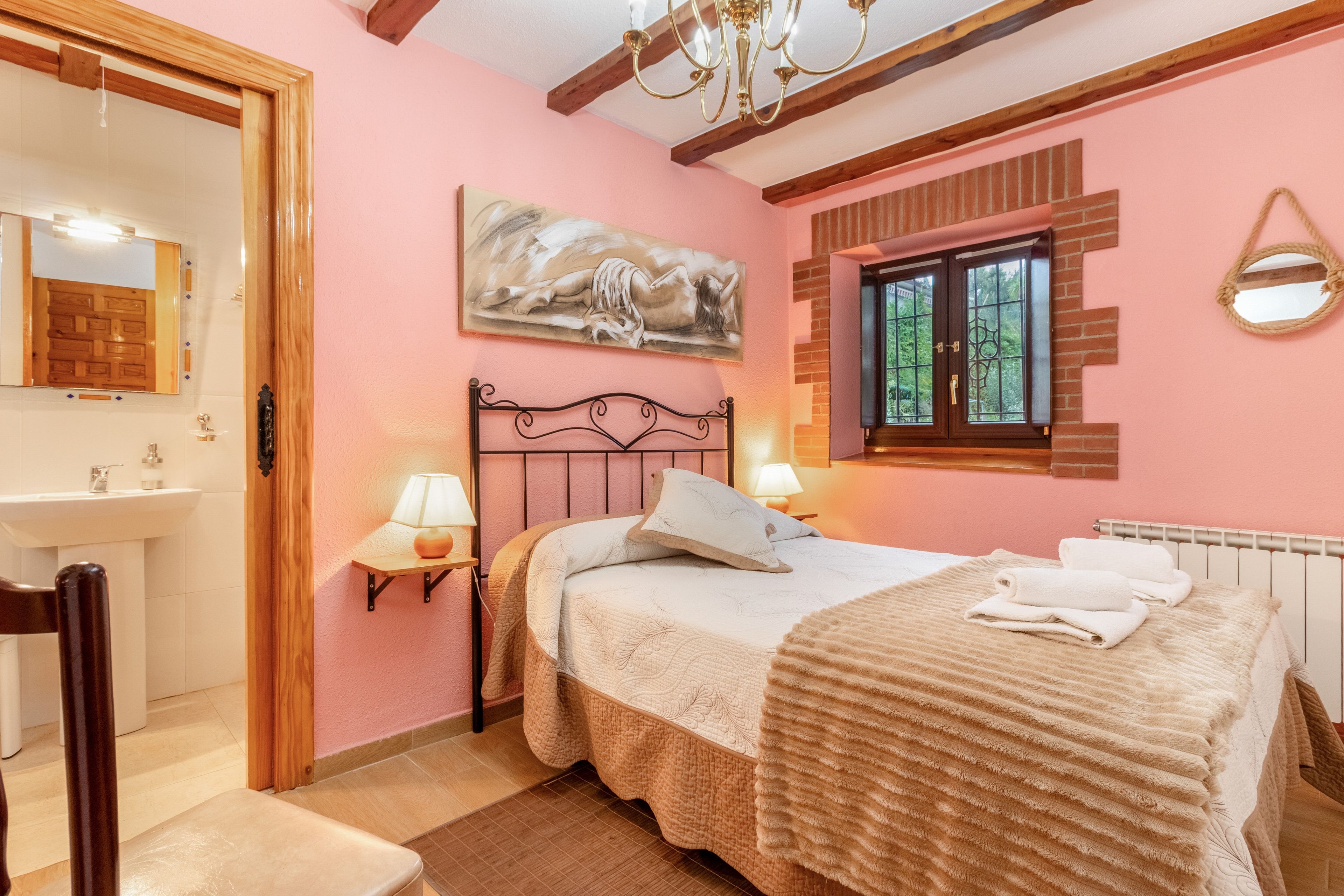 A bedroom with a bed, bedside lamps, a painting, a window, and a radiator.