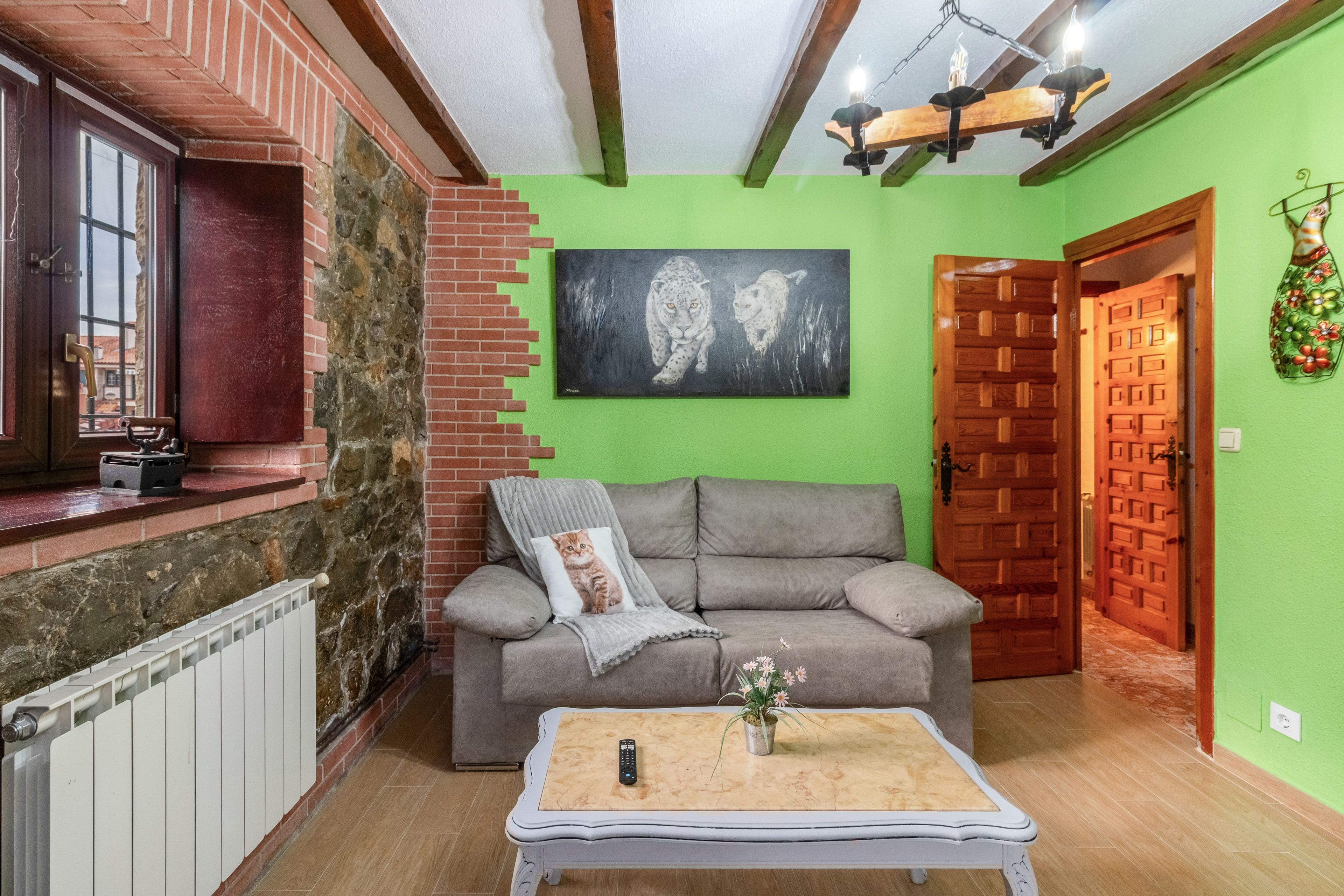 A living room with a grey sofa, a painting of leopards, a radiator, and a wooden door.