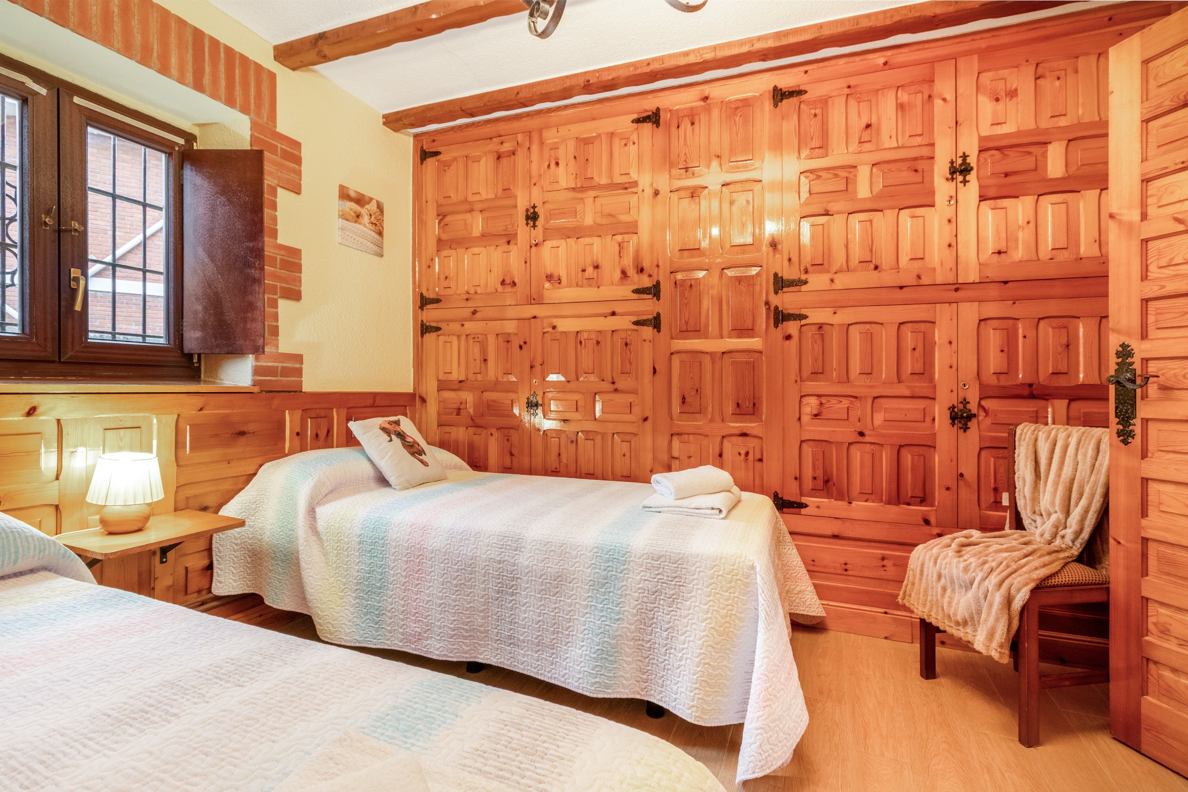 A room with two beds, a wooden wardrobe, a chair, and a window.