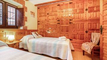 A room with two beds, a wooden wardrobe, a chair, and a window.