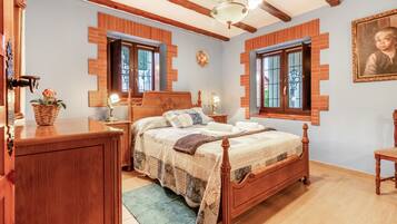 Een slaapkamer met een houten bed, een dressoir, een nachtkastje, een lamp en een lijst met een afbeelding aan de muur.