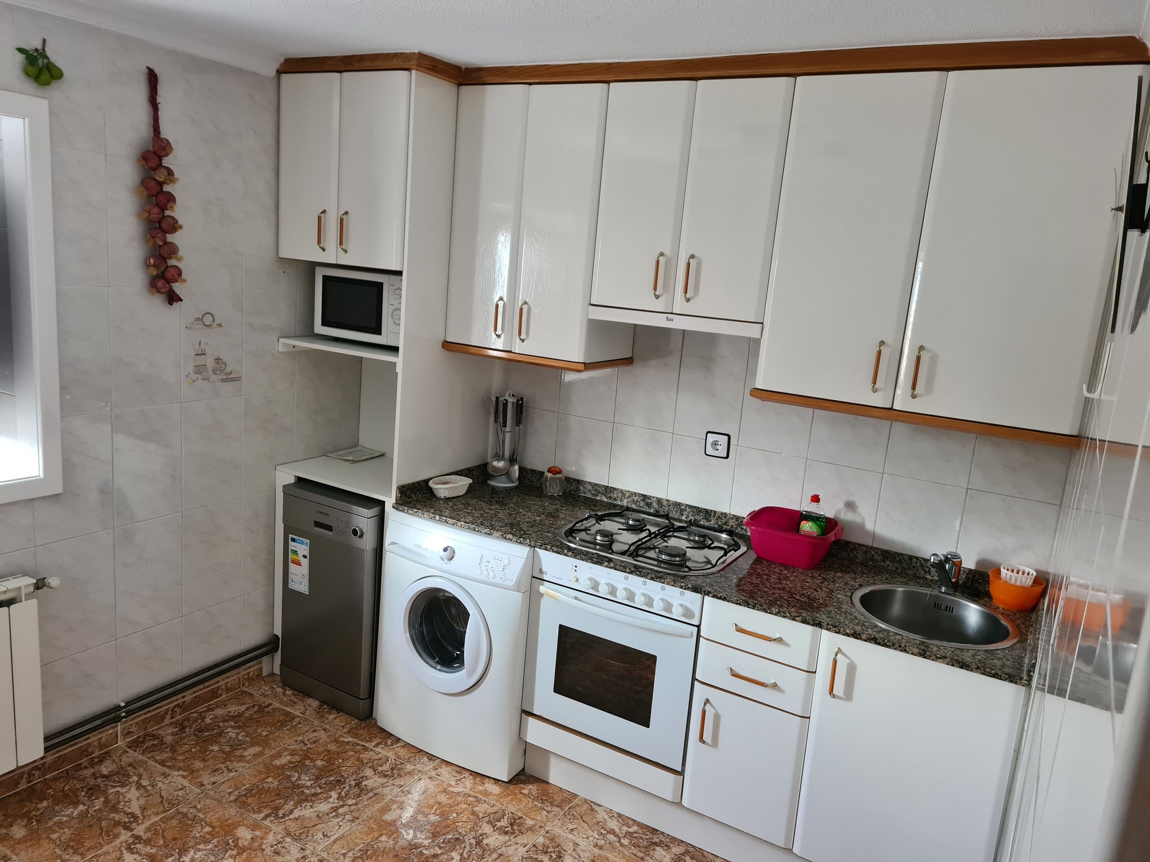 A compact kitchen with white cabinets, a washing machine, a microwave, and a gas stove.