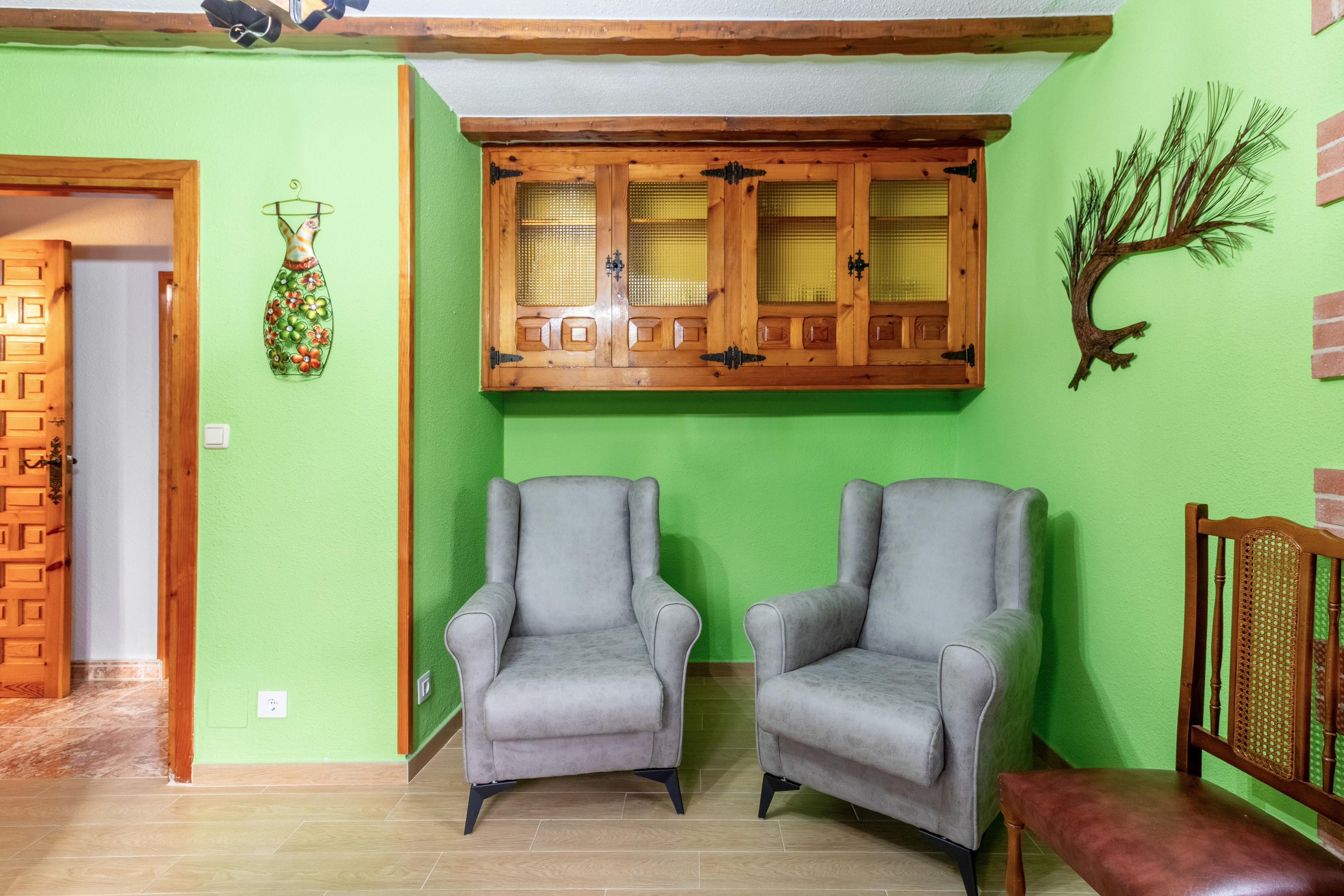 A room with two grey armchairs, a wooden cabinet with glass doors, and a green wall.