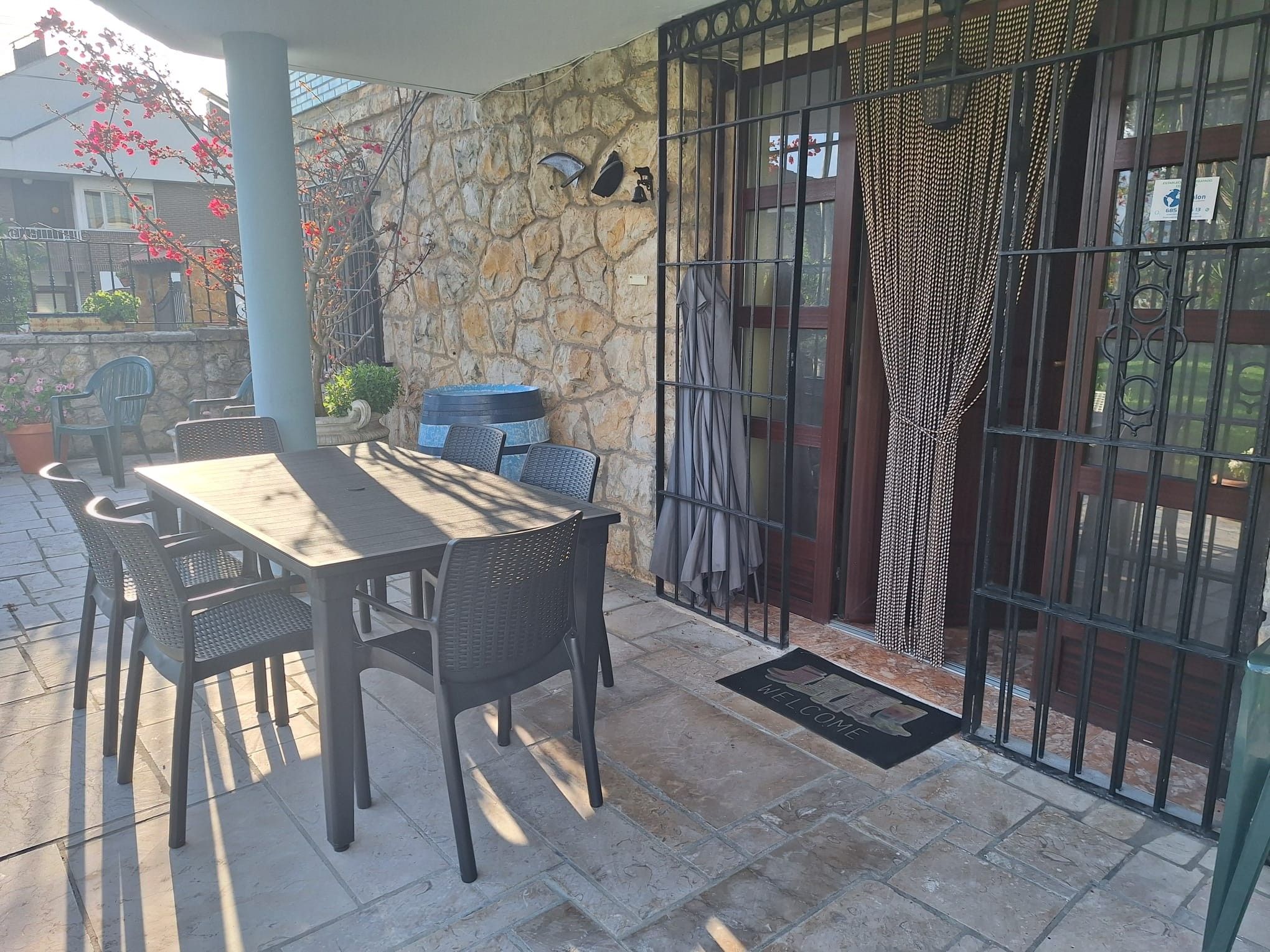 Un patio exterior con muro de piedra, una mesa con sillas y una reja metálica.