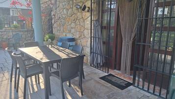 Un patio exterior con muro de piedra, una mesa con sillas y una reja metálica.