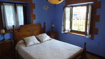 A bedroom with a wooden bed, a nightstand, a lamp, a window with bars, and a ceiling fan.