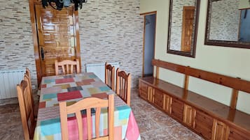 A dining area with a wooden table, chairs, a patterned tablecloth, a chandelier, and a mirror on the wall.